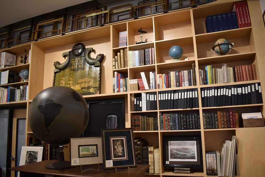 A gallery wall filled with antique maps, framed prints, books and globes