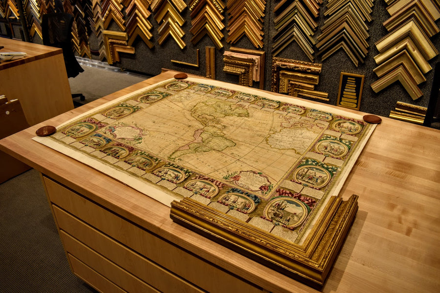 An antique world map being designed with gilded picture frame moulding samples